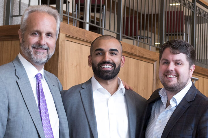 A professor and two business students, all in suits, standing shoulder to shoulder.